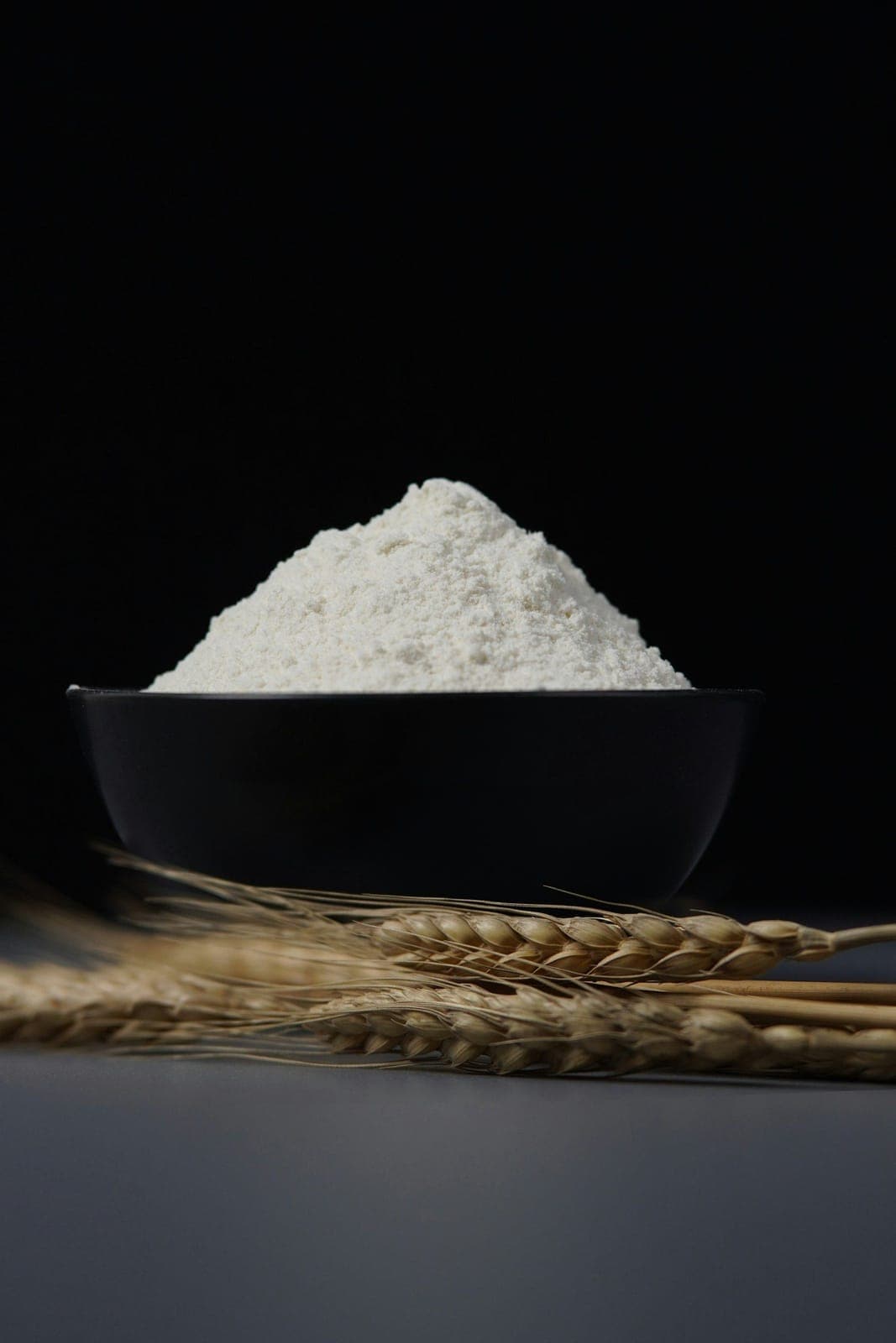 A bowl of milled flour beside ears of wheat